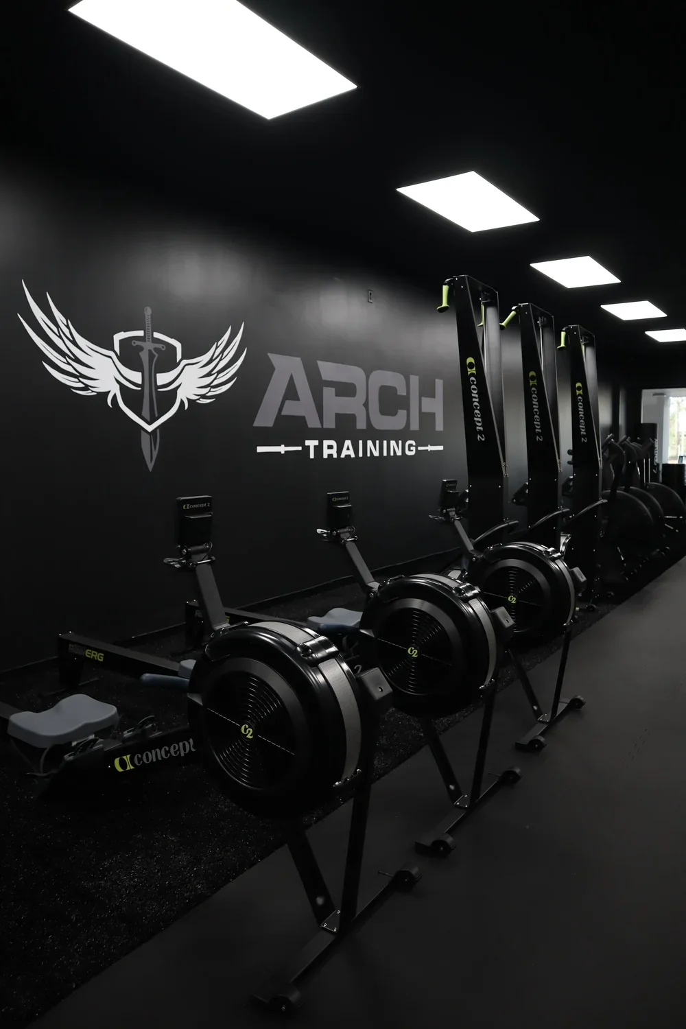The ARCH Training logo on the wall above a row of Concept2 rowing ergs at ARCH Training Freehold